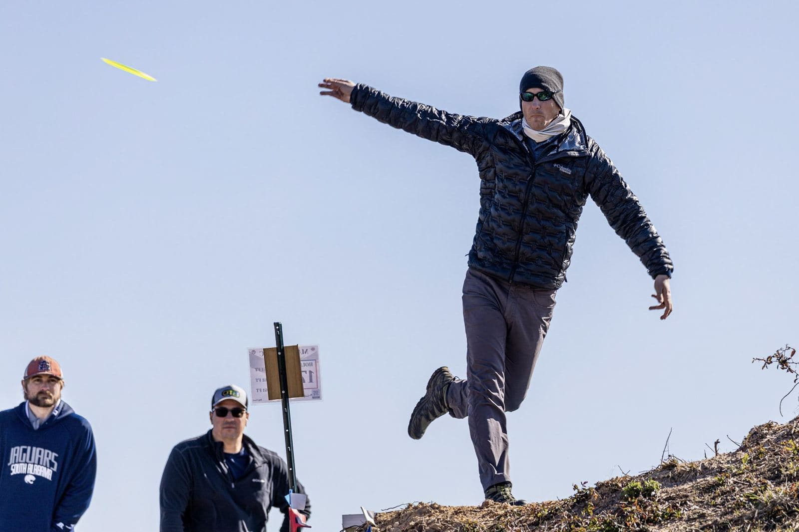 A player mid-air off a mound during a winter drive, the disc already in flight against a pale sky.