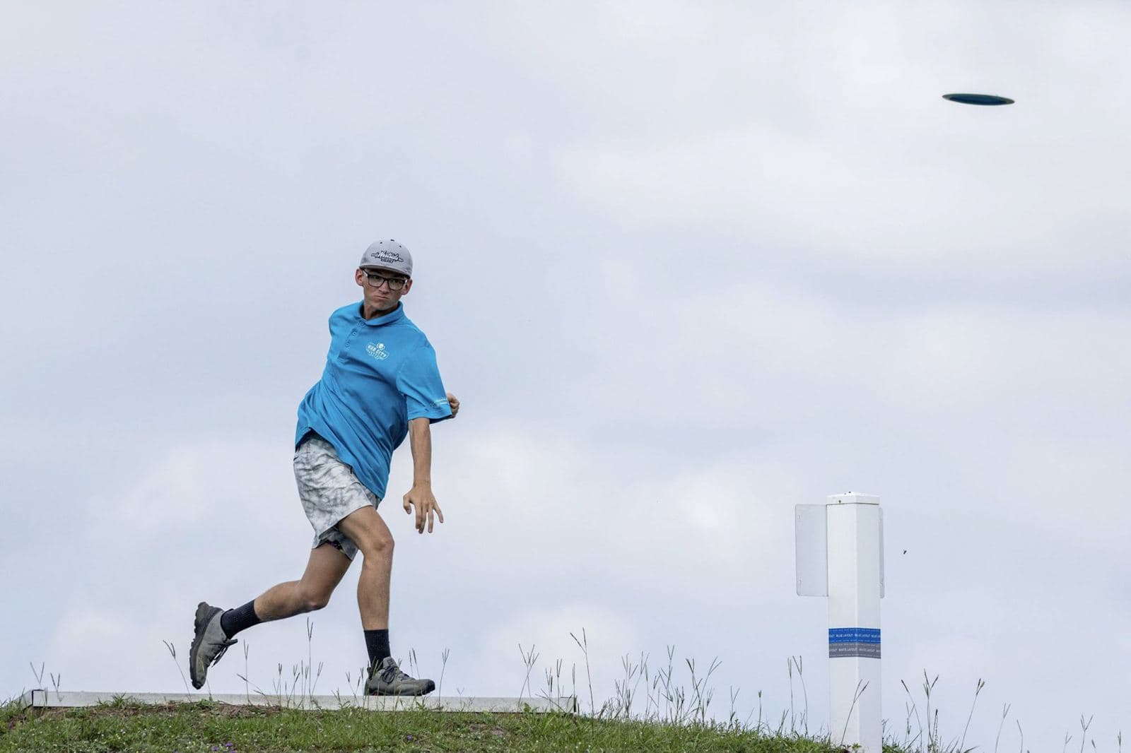 A player in blue drives from a concrete tee, the disc high against the sky.
