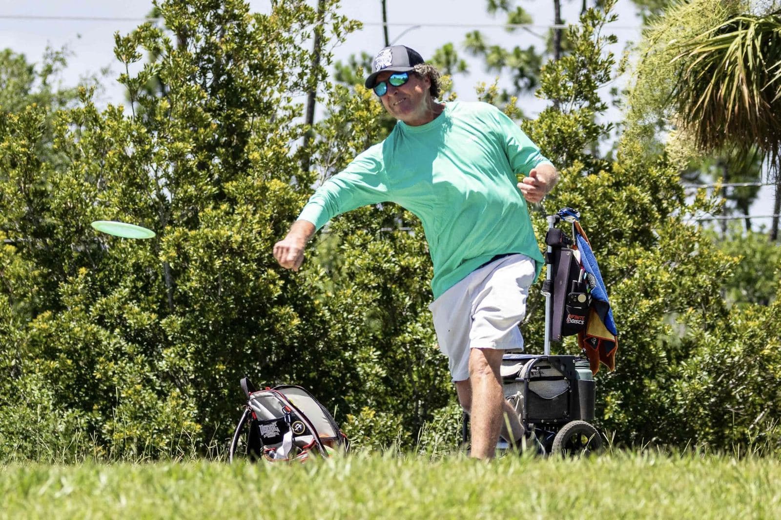 A player in a green shirt releases a backhand drive in front of a hedge.